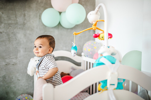 Cute little boy standing in his crib looking surprised.