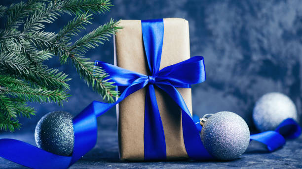 istock Beautiful gift box with blue ribbon, tree branches and balls close up 1186127742