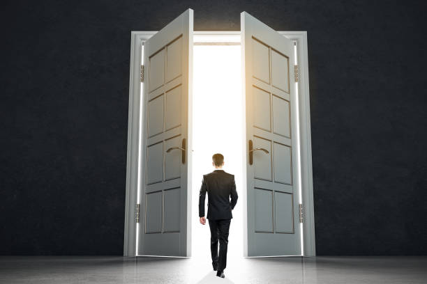 istock New life beginning concept with businessman entering open white doors in abstract bright space. 1186130296