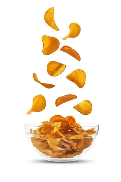 Delicious potato crisps are falling down in a glass bowl, isolated on white background with copy space for your text or images. Crispy, palatable chips. Shadow. Advertising concept. Close-up shot.