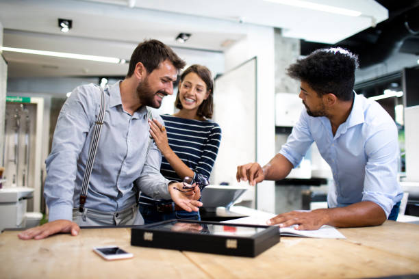 istock Store salesman having a discussion with young shopping couple while leaning over the table with a catalog in the store 1186130623
