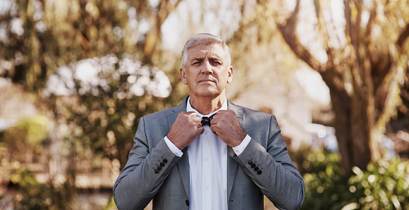 Cropped portrait of a handsome mature bridegroom adjusting his necktie while preparing for his wedding outdoors