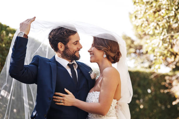 Cropped shot of an affectionate young newlywed couple smiling at each other while covering themselves with a veil on their wedding day