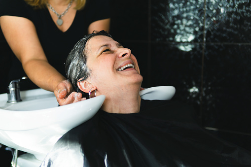 Beauty and people concept - Happy woman washing hair at a hairdressing salon before doing hairstyle.