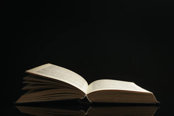 istock One open old book on a glass table. Beautiful dark background.. 1186136255