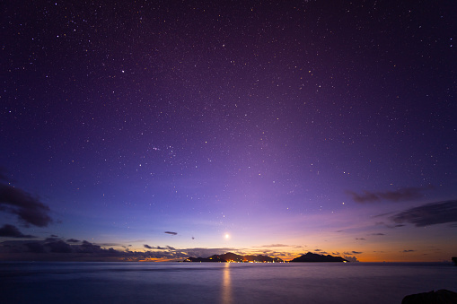 night sky with many stars and shining moon over tropical island