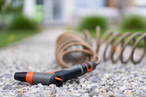 spray pistol and garden hose for watering irrigation on gravel path outdoors shallow focus on foreground background blurred