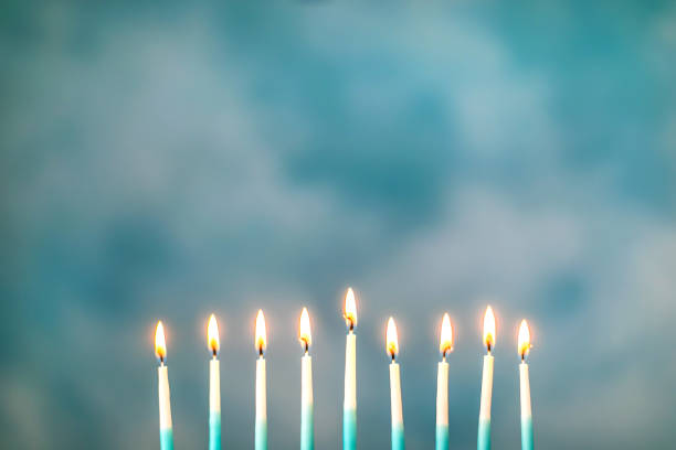 a silver menorah for the jewish holiday hanukkah with burning glowing eight candles on fire lit up on a blue background with copy space - hanukkah menorah candle blue imagens e fotografias de stock