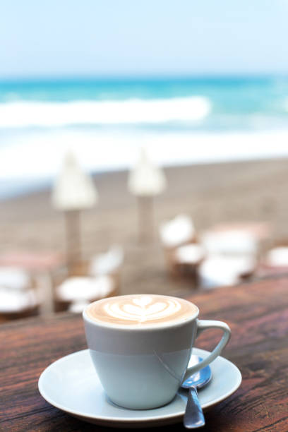 Cup of hot cappucino on wooden table background with ocean view background. Vacation concept.