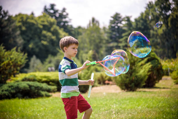 niño jugando con su juguete de burbujas de jabón en el parque. actividad infantil. concepto primaveral - child dancing preschooler outdoors fotografías e imágenes de stock