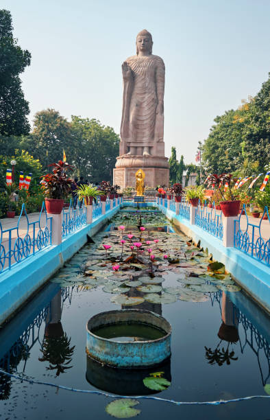 Giant Buddha statue at Wat Thai Temple & Monastery of Sarnath, Uttar Pradesh, India Gautam Buddha statue in Deer Park, Sarnath Excavated Site, Near Varanasi, Uttar Pradesh. Gathering of tourists can be seen.
This place is one of the four key sites on the Buddhist circuit – along with Bodhgaya, Kushinagar and Lumbini in Nepal – and attracts followers from around the world.  Gautama Buddha first taught the Dharma (teaching of Buddhism) to his disciples, here in Sarnath. Indian Archaeological Survey has excavated the site and recovered the lost history from the past.
Photo taken at Sarnath, Uttar Pradesh, India on 11/18/2018. sarnath stock pictures, royalty-free photos & images