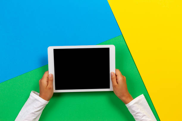 istock Kid hands with tablet computer on yellow, blue and green background 1186156554