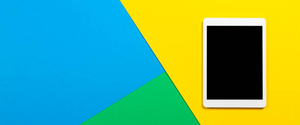 Digital tablet computer on light blue, green and yellow background. Top view