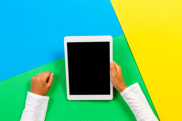 istock Hands holding tablet computer on yellow, blue and green background. Top view 1186156794
