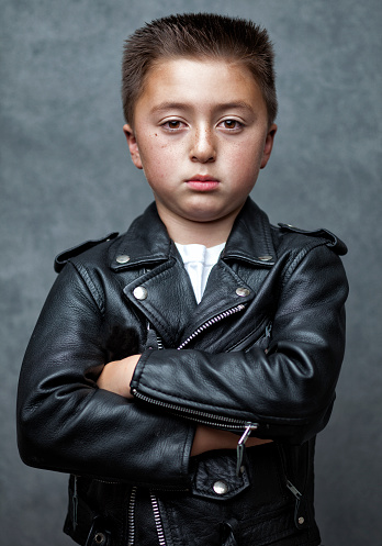 Handsome mixed race Asian Caucasian boy with a flattop flat top hair cut with arms crossed wearing a black leather motorcycle jacket and white shirt in front of gray background