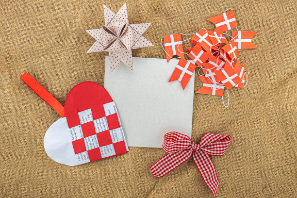 Overhead studio image of a blank greeting card with traditional Danish Christmas decoration elements (folded julestjerne, flettet julehjerte and dannebrog flagguirlande) , on a hessian sack background