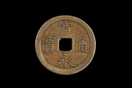 A close up image of a bronze, Chinese cash coins, shot close up in macro against a black background