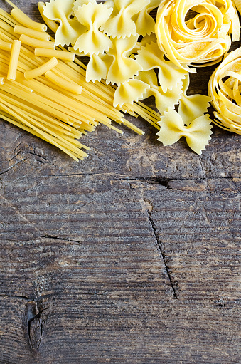 Variety of types and shapes of Italian pasta on old wooden background from above. Italian cuisine food concept and menu design. Dry pasta background. Top view. Flat lay. Copy space.