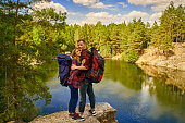 Couple of tourists exploring a new places. A handsome couple with backpack on nature near the lake at forest background.