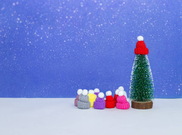 istock Green christmas tree in red cap under the snow with multicolored caps on light blue background 1186177497