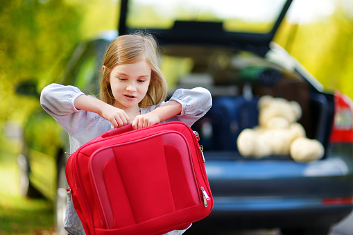 Adorable little girl with a suitcase leaving for a car vacation with her parents