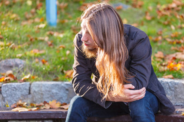 istock Man long hair sitting on bench in autumn park 1186181861