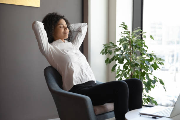 femme d'affaires africaine calme détendant s'asseyant sur le fauteuil dans le hall de bureau - yoga business women indoors photos et images de collection