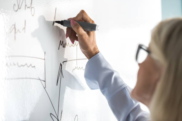 Female entrepreneur 50s writing plan on white board in office