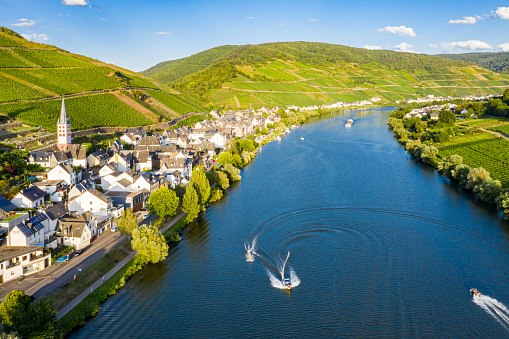 Hills with vineyards and church in Merl village of Zell (Mosel) town, Rhineland-Palatinate, Germany. Water skiing, barges, speedboats on the Moselle river meander