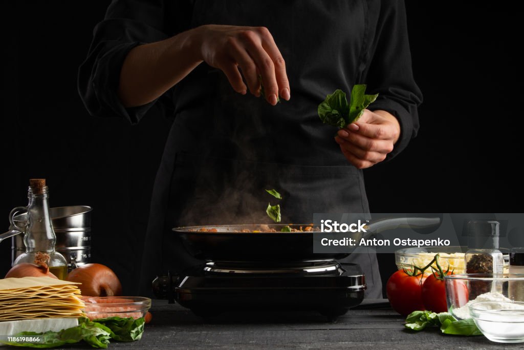 Cooking by a chef Italian lasagna, frying a dressing in a frying pan. And sprinkling with basil. Freezing in motion. Cooking, homemade recipe book. Delicious and healthy food. Chef Stock Photo