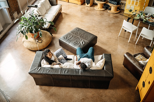 African couple of roommates sitting in the living room, drinking coffee and talking, high angle view.  They are friends who sharing living space