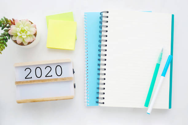 istock 2020 on wood box, blank notebook paper on white marble table background, 2020 new year mock up, template with copy space for text, top view 1186218935