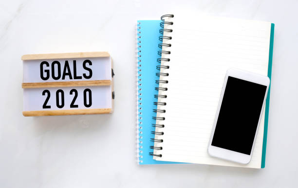 istock 2020 on wood box, blank notebook paper and smart phone with blank screen on white marble table background, 2020 new year mock up, template with copy space for text, top view 1186218985