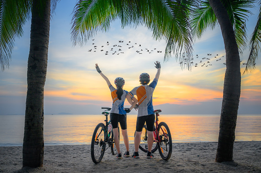 couple lover riding bicycle along the sea beach under coconut trees at sunset, relaxation at the end of the day
