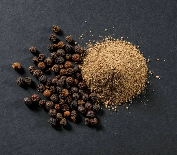 whole and ground black allspice peppercorns close-up on gray background view from above