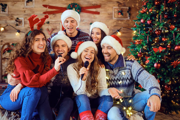 Laughing friends celebrating Christmas in karaoke Happy men and women in Santa hats having fun in karaoke singing together and celebrating Christmas holiday traditional song stock pictures, royalty-free photos & images