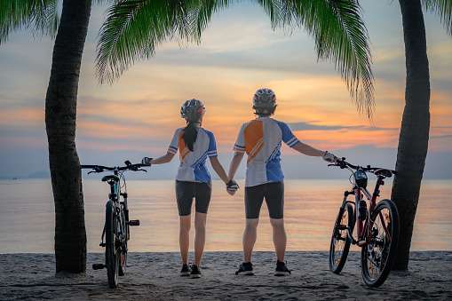 couple lover riding bicycle along the sea beach under coconut trees at sunset, relaxation at the end of the day