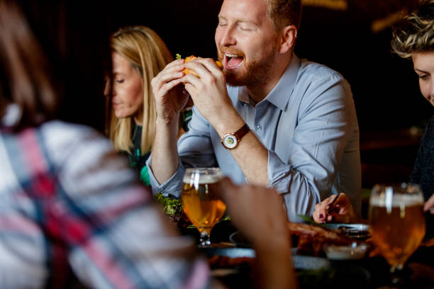 istock Young redhead man with friends in a pub eating hamburger with pleasure 1186250057