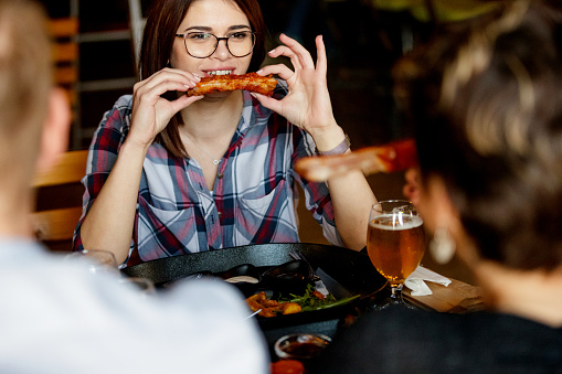 Young woman sitting in a pub with friends and eating sparerib held in hands