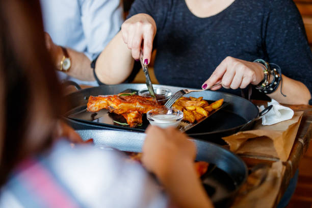 Sitting in a pub and cutting ribs with cutlery, served with potatoes and sauce on a tray