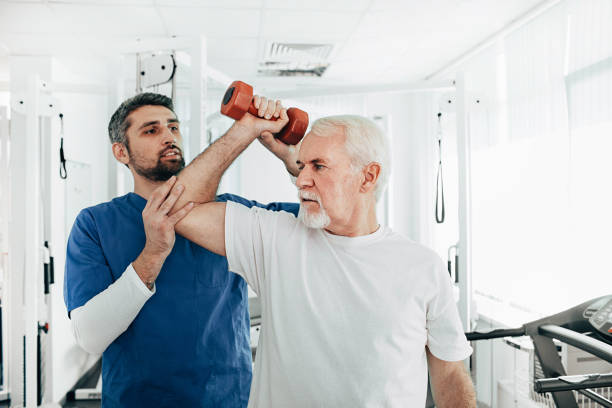 senior man lift a dumbbell, he doing treatment exercise with his physiotherapist. Physio treatment at rehab center senior man lift a dumbbell, he doing treatment exercise with his physiotherapist. Physio treatment at rehab center occupational therapy photos stock pictures, royalty-free photos & images
