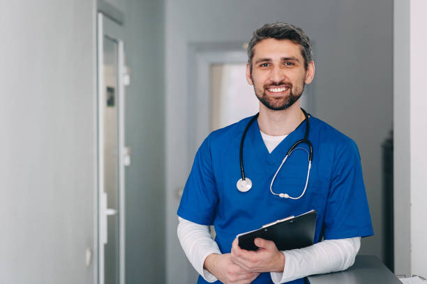 male nurse with stethoscope standing at clinic. He is smiling and looking at the camera. male nurse with stethoscope standing at clinic. He is smiling and looking at the camera. general practitioner photos stock pictures, royalty-free photos & images