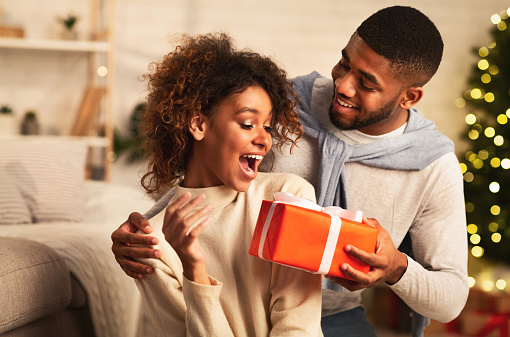 Xmas surprise. Afro man giving Christmas present to girlfriend, celebrating holidays together