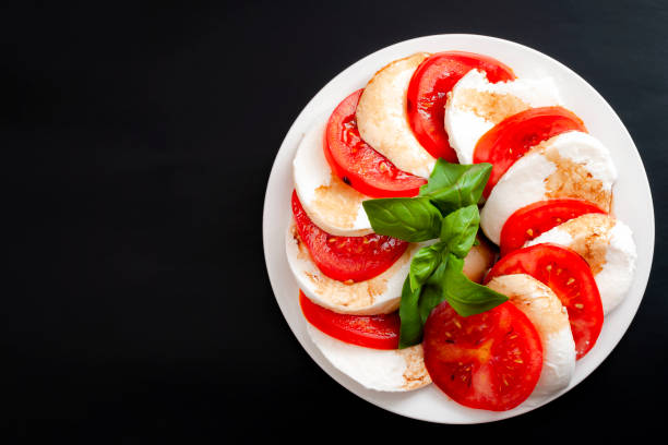 cucina mediterranea, cibo vegetariano fresco e concetto di arte culinaria italiana con insalata caprese a base di mozzarella, pomodori e foglie di basilico isolate su sfondo nero con spazio di copia - plate salad leaf vinegar foto e immagini stock