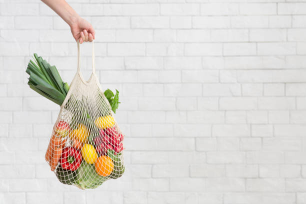 Woman holding fresh vegetables over white bricks wall in eco shopping bag Rejection of plastic. Woman holding fresh vegetables over white bricks wall in eco shopping bag, copy space reusable bag stock pictures, royalty-free photos & images