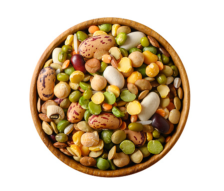 Various dried legumes: lentils bean pea chickpea in a wooden cup top view isolated on white.