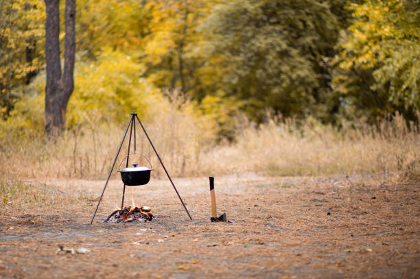 istock Campfire with camping tools such as axe and hanging pot over fire. Secluded relaxation in autumn forest away from bustle of city 1186276380