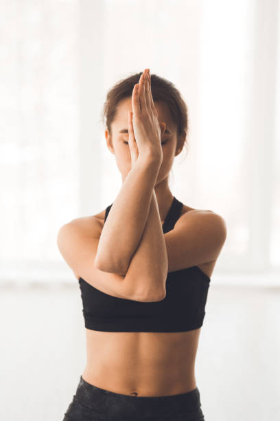 Woman with crossed arms performing yoga exercise Eagle pose. Woman with crossed arms performing yoga exercise over white window, crop twist pose stock pictures, royalty-free photos & images