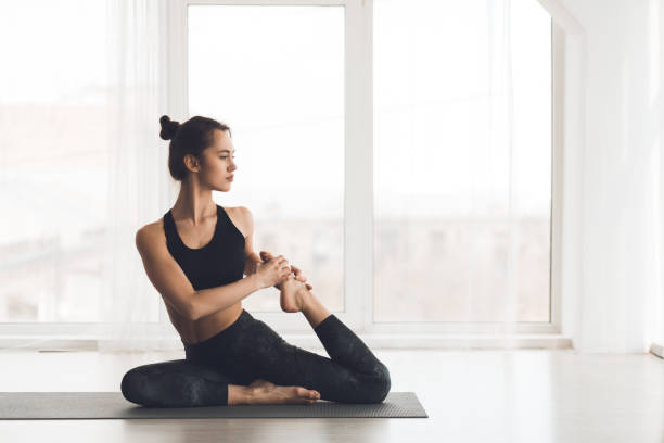 Yoga concept. Sporty woman stretching on mat Yoga concept. Sporty woman stretching on mat over light panoramic windows, free space studio yoga adult action stock pictures, royalty-free photos & images