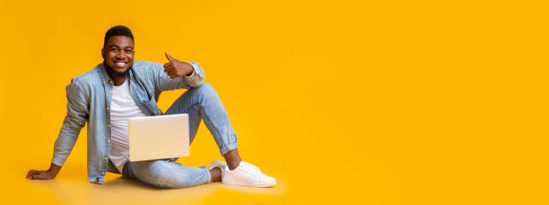 istock African man sitting with laptop on floot, gesturing thumb up 1186283182
